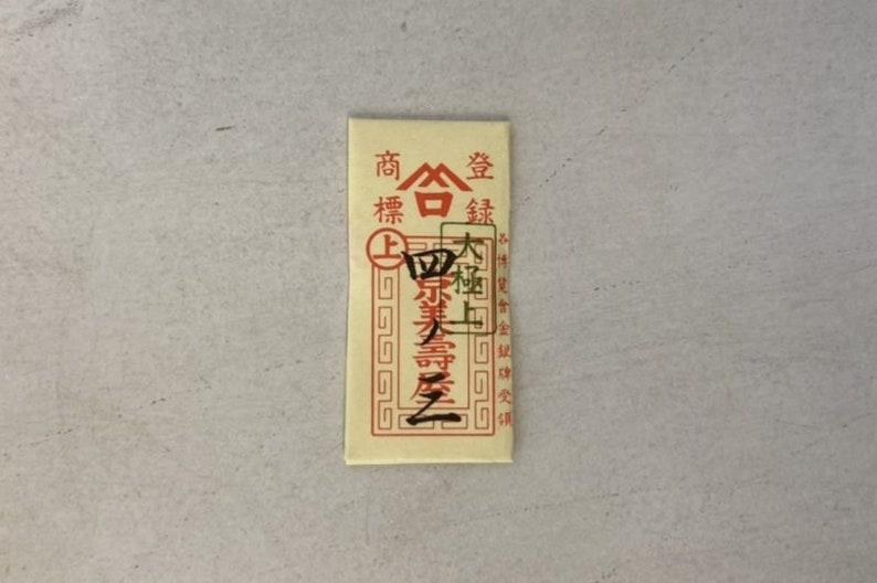 May include: A red and white paper envelope with Chinese characters that read "Shang Hai Jin", which translates to "Shanghai Gold". The envelope has a red border and a gold seal with a Chinese character.