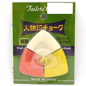 May include: A triangular sewing chalk holder with three colours: white, orange, and yellow. The holder is labelled "人物印チョーク" which translates to "Person Mark Chalk" in English. The package also says "色パック" which translates to "Colour Pack" and "ピック付き" which translates to "Pick Included". The package is labelled "Made in Japan".