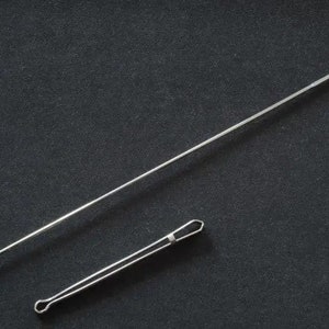 May include: Two silver metal crochet hooks on a dark gray surface. One hook is long and straight with a hook at the end. The other is shorter with a loop at the end. The hooks are used for crocheting.