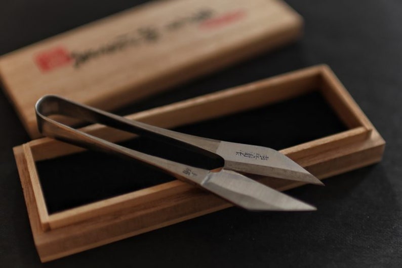 May include: A pair of silver-coloured, sharp-pointed scissors with a wooden box. The scissors have a Japanese inscription on the blade that reads "Tsubame".