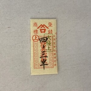 May include: A small, rectangular, cream-colored paper packet with red Chinese characters that read "Shang Hai Jin", which translates to "Shanghai Gold". The packet has a red border and a gold seal with a white triangle inside.