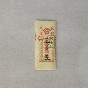 May include: A small, rectangular, cream-colored paper packet with red and green text. The text reads "高林金" and "大福 上等" in Japanese.