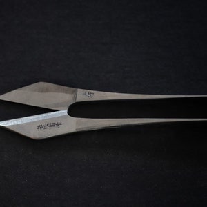 May include: A pair of silver-coloured fabric shears with a pointed tip and a curved handle. The shears have Japanese text on the blades.