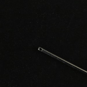 May include: A silver surgical needle with a small eye at the top, against a black background.