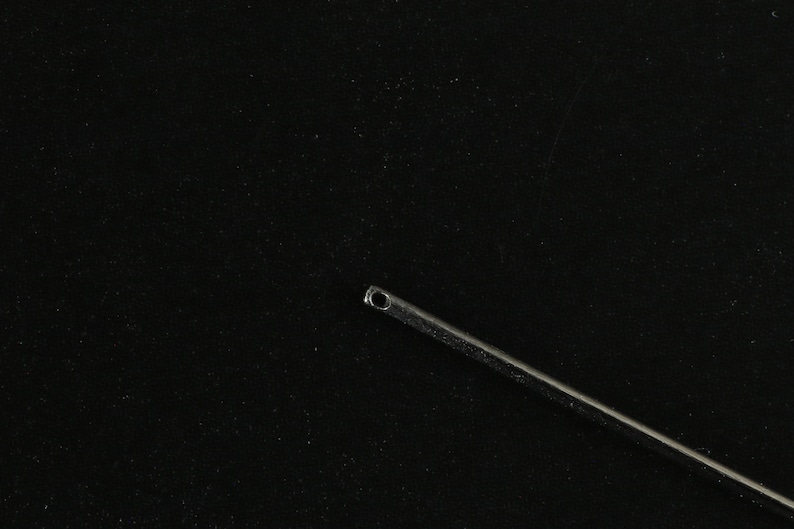 May include: A silver surgical needle with a small eye at the top, against a black background.