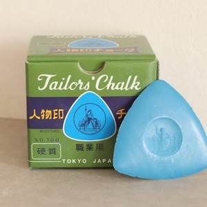 May include: A green box with the text "Tailors' Chalk" and a blue triangle-shaped tailor's chalk with a logo on it. The box has Japanese text on it, including "人物印" and "職業用".