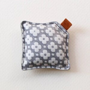 May include: A small grey and white patterned cushion with a brown leather tag. The cushion is filled with a soft material and has a decorative stitch around the edges.