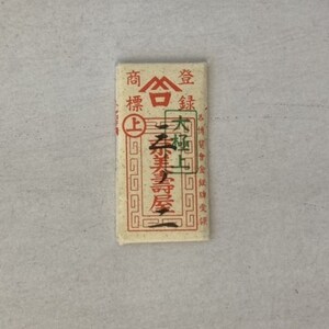 May include: A small, rectangular, cream-colored paper packet with red Chinese characters printed on it. The packet is labeled "商標登録" which translates to "Trademark Registration".