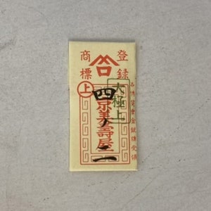 May include: A small, rectangular, cream-colored paper packet with red and black Chinese characters. The text reads "商標登録" which translates to "Trademark Registration".