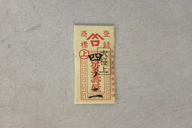May include: A small, rectangular, cream-colored paper packet with red and black Chinese characters. The text reads "商標登録" which translates to "Trademark Registration".