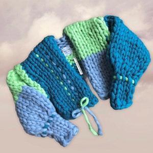 May include: A chunky knit sweater in shades of blue and green. The sweater features a color-blocked design with sections of light blue, teal, and lime green. The sleeves are thick and the sweater has a tie closure. The tag reads "SUBOIKNIT".