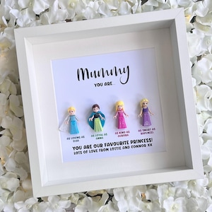 May include: A white frame with a white mat and a white background. The frame contains a message that reads "Mummy You Are..." and four small plastic figurines of Disney princesses. The text below the figurines reads "As loving as Elsa, As loyal as Anna, As kind as Aurora, As smart as Rapunzel. You are our favourite princess! Lots of love from Lottie and Connor xx."