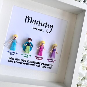 May include: A white frame with a white background and the text "Mummy You Are..." in black. There are five small plastic figures of Disney princesses in the frame. The text below the figures reads "You are our favourite princess! Lots of love from Lottie and Connor xx."