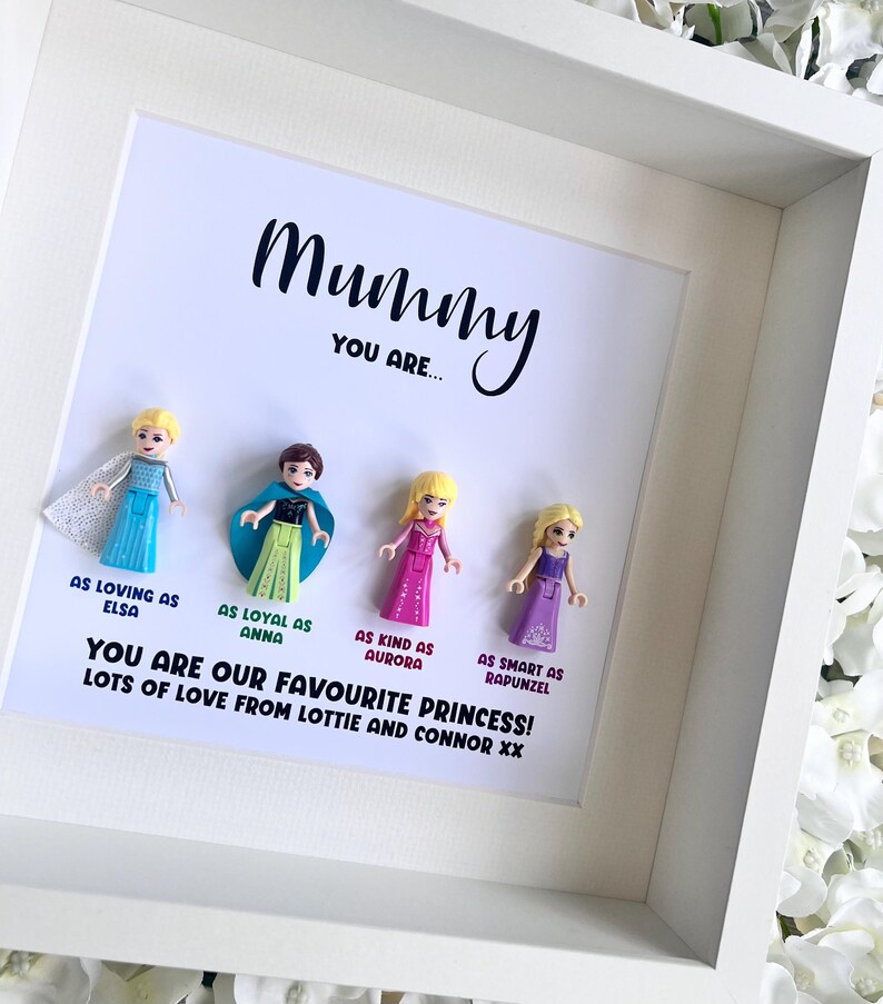 May include: A white frame with a white background and the text "Mummy You Are..." in black. There are five small plastic figures of Disney princesses in the frame. The text below the figures reads "You are our favourite princess! Lots of love from Lottie and Connor xx."