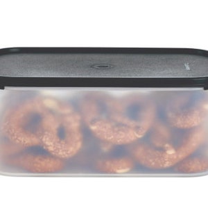 Peut inclure: Un récipient rectangulaire en plastique transparent avec un couvercle noir. Le récipient est rempli de bretzels bruns.