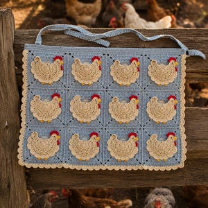 May include: A light blue crocheted apron featuring a grid of twelve beige chicken motifs. Each chicken has a red comb and yellow beak. The apron has a scalloped beige border along the bottom and sides, with two long ties at the top for fastening.