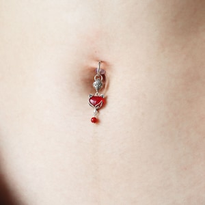 May include: A silver belly button ring with a red heart charm and a small red bead dangling from the bottom.