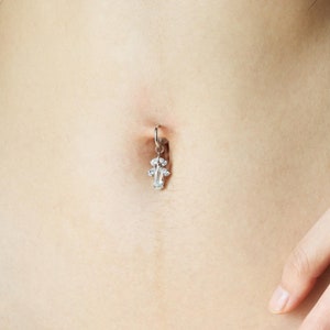 Puede incluir: Un piercing de ombligo plateado con un dije de cristal transparente en forma de cruz.