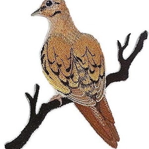 Puede incluir: Parche bordado de una paloma marrón y blanca posada en una rama. La paloma tiene un diseño detallado con plumas marrones y blancas. La rama es negra.