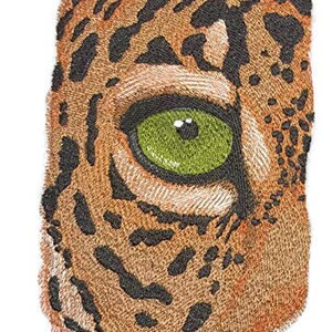 May include: Close-up of a brown and black embroidered patch depicting a jaguar's eye with a green iris. The patch is designed to look like fur.