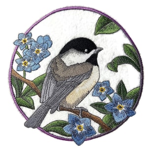 Peut inclure: Patch brodé représentant un mésange à tête noire perché sur une branche avec des fleurs bleues de myosotis. Le patch est circulaire avec une bordure violette et un fond blanc.