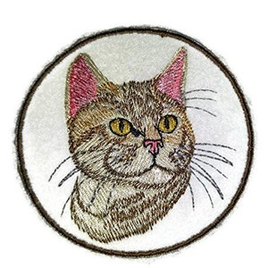 May include: Embroidered patch of a brown tabby cat with pink ears, looking to the right, against a white background.