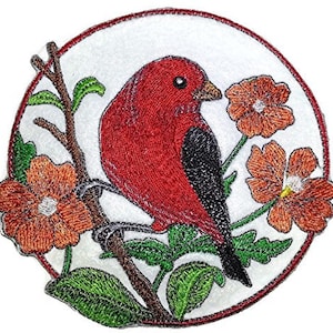 Peut inclure: Patch brodée thermocollante représentant un oiseau rouge aux ailes noires perché sur une branche avec des fleurs orange. Le patch est circulaire et a un fond blanc.
