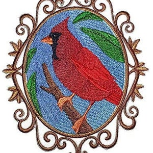 May include: Embroidered patch featuring a vibrant red cardinal perched on a branch within an oval frame. The bird has a black beak and is set against a blue background with green leaves. The frame is ornate with a gold-brown filigree design.