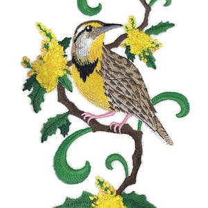 May include: Embroidered patch featuring a brown and yellow bird perched on a branch with green leaves and yellow flowers. The bird has a black eye stripe and a yellow breast.