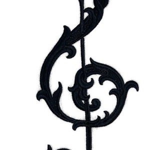 May include: Black embroidered treble clef with intricate floral details. The treble clef is a musical symbol used to indicate the pitch of notes.
