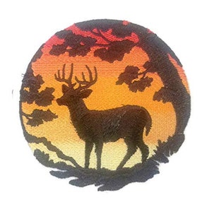 May include: Embroidered patch depicting a silhouette of a deer standing in a woodland setting with a sunset backdrop. The deer is facing left and has large antlers. The background is a gradient of orange, yellow, and red.