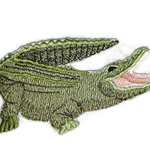 May include: Green embroidered alligator patch with an open mouth, showing white teeth and a pink tongue. The alligator is facing right and has a textured, scaly appearance.