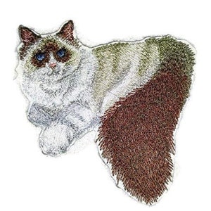 Op de afbeelding: Gestikt patch van een witte en bruine Ragdoll-kat met blauwe ogen. De kat ligt met zijn staart om zijn lichaam gekruld.