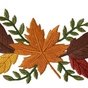 May include: Embroidered autumn-themed design featuring a large orange maple leaf, various brown, red, and yellow leaves, green sprigs, two blue birds, and several brown acorns. The design is set against a white background.