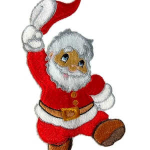 以下が含まれることがあります： 赤いスーツ、白いトリム、白い帽子をかぶった、漫画のサンタクロースの刺繍アイロン接着パッチ。彼は右手を上げて帽子を持ち、笑顔を見せています。