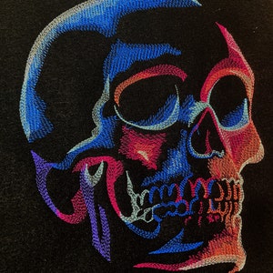 May include: A colourful embroidered skull design with blue, pink, and purple thread on a black fabric background.