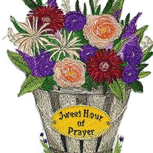 以下が含まれることがあります： 木製のバケツに花束が刺繍されたパッチ。花はピンク、赤、紫、白の色合いです。バケツには「Sweet Hour of Prayer」という文字が書かれた黄色の楕円形のタグが付いています。