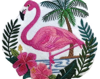 Könnte beinhalten: Ein gestickter Aufnäher mit einem leuchtend rosa Flamingo, der auf einem Bein steht. Das Motiv zeigt eine braune Palme, dunkelgrüne tropische Blätter und zwei große rosa Hibiskusblüten mit gelben Mitten auf weißem Hintergrund.