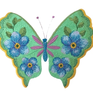 May include: An embroidered butterfly patch featuring a light green base with a yellow scalloped border. The wings are decorated with blue flowers, yellow centers, and green leaves. The central body is blue with purple accents and two thin antennae.