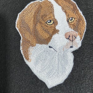 May include: Embroidered image of a brown and white dog's head with a white background. The dog has brown fur around its eyes and nose.