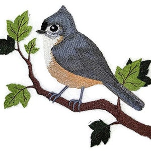 May include: Embroidered design of a tufted titmouse perched on a branch with green leaves. The bird is gray and brown with a white breast.