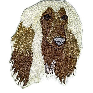 May include: Embroidered patch of an Afghan Hound dog with white and brown fur. The dog is looking to the right with its tongue out.