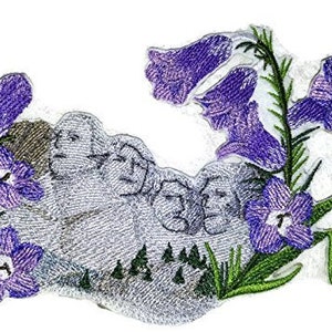 May include: Embroidered patch depicting a grey stone sculpture of four faces surrounded by purple and white flowers. The flowers are bell-shaped and have green stems and leaves.
