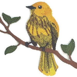 May include: Yellow bird with brown stripes perched on a branch with green leaves. The bird is facing left and has a small beak.