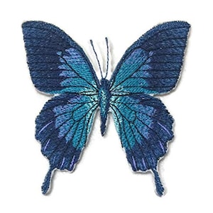Könnte beinhalten: Gestickter Schmetterlingsaufnäher in Blau- und Türkistönen. Der Schmetterling hat detaillierte Flügelmuster und zarte Fühler. Dieser dekorative Aufnäher kann auf Stoff aufgebügelt oder aufgenäht werden.