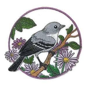 Peut inclure: Patch brodée thermocollante représentant un oiseau gris et noir perché sur une branche avec des fleurs violettes. L'oiseau est entouré de feuilles vertes et d'un fond blanc.
