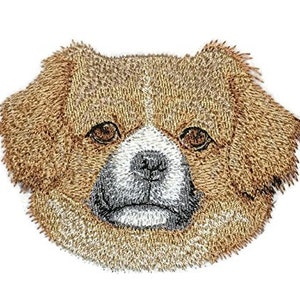 Puede incluir: Parche bordado de un perro pequinés marrón y blanco con un pelaje esponjoso. El perro está mirando directamente al espectador.