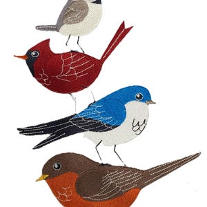 Puede incluir: Imagen bordada de cuatro pájaros coloridos apilados uno encima del otro. Los pájaros incluyen un cardenal rojo, un azulejo, un petirrojo marrón y un pequeño pájaro gris. Los pájaros están representados con puntadas detalladas sobre un fondo blanco.