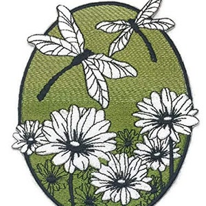 May include: An embroidered patch with a green background featuring two white dragonflies and white flowers. The dragonflies are flying over the flowers, which are in bloom.