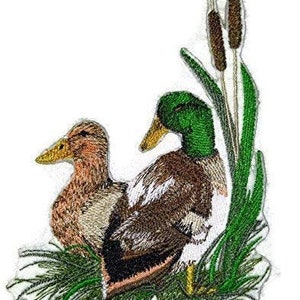 May include: Embroidered patch featuring two mallard ducks in a green grassy area with cattails. The ducks are brown and green with detailed stitching.